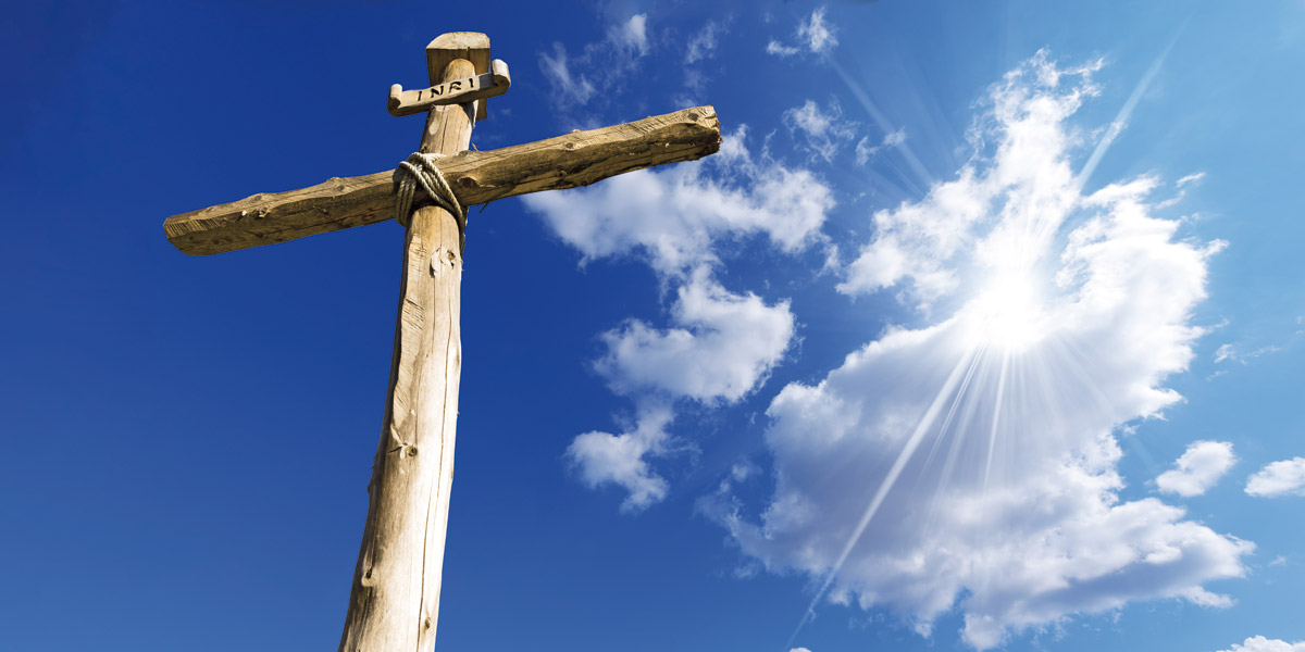 Ein Holzkreuz vor blauem Himmel und Sonne